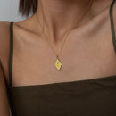 Gold necklace with a diamond-shaped pendant on a person wearing a brown top.