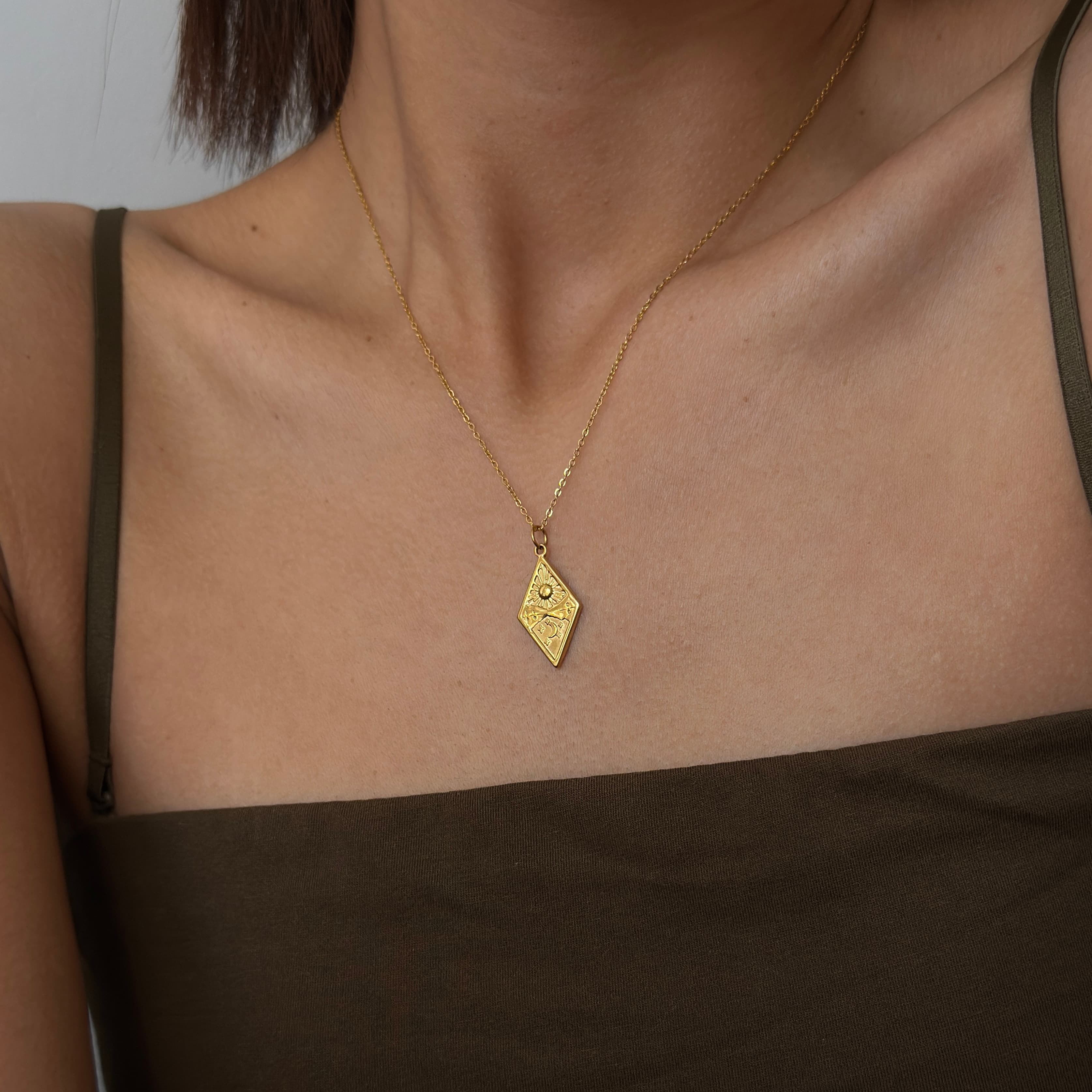 Gold necklace with a diamond-shaped pendant on a person wearing a brown top.